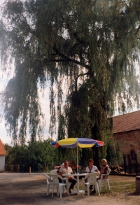 Anna Šlechtová with her mother and a photographer in front of the mourning willow that her mother planted before they were moved out from the farm no. 15, 1992, Neratov.
